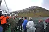 Turister på et båtdekk ser mot et bratt fjell ved en fjord.