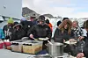 Utendørs matservering med mennesker i vinterklær foran snødekte fjell.