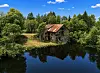 Forfallen trebygning ved et stille tjern, omgitt av frodig skog under blå himmel.