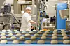 Deigemner på samlebånd i et industribakeri med en baker og produksjonsutstyr i bakgrunnen.